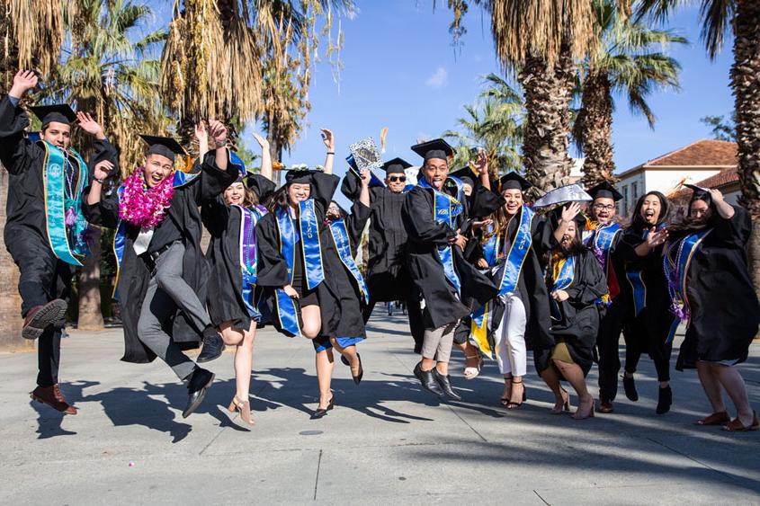 菠菜网lol正规平台 graduates jumping up in the air.